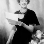 Black and white photograph of Caroline Klein Simon seated and reading a folded paper document.