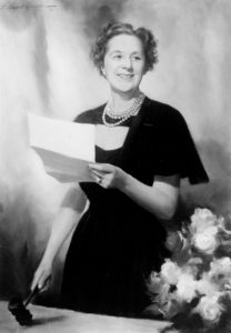 Black and white photograph of Caroline Klein Simon seated and reading a folded paper document.