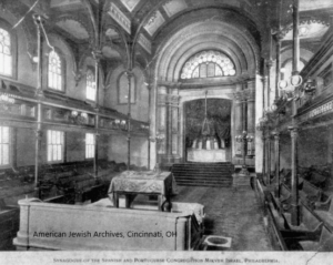 Image of the inside of Mikveh Israel, including central bima, ark, and separated, gender-based seating on different levels.