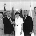 Rabbi Julie Schwartz (middle), in uniform. Two men stand on either side of her. Four flags are behind them, including the U.S. flag.