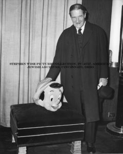 Black and white photograph of Rabbi Stephen S. Wise standing in an overcoat beside a doll.